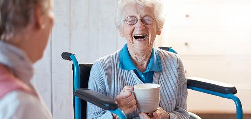 Older lady in wheelchair, drinking tea and laughing