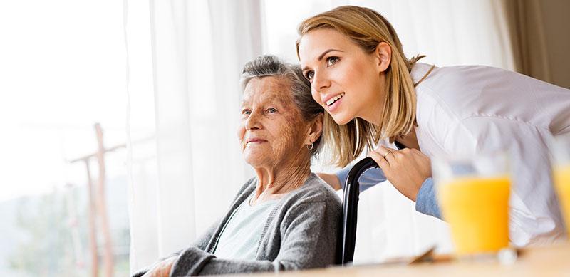 Care worker pushing elderly lady in wheelchair and looking out window