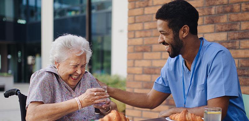 Care worker sitting in garden with elderly lady in wheel chair. Laughing over joke